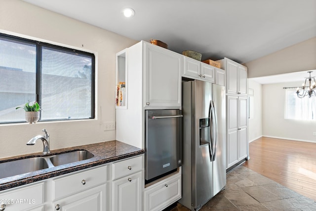 kitchen with lofted ceiling, sink, white cabinets, stainless steel fridge, and an inviting chandelier