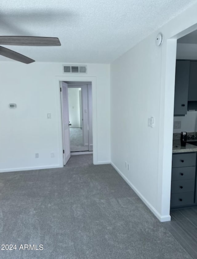 spare room with ceiling fan, dark carpet, and a textured ceiling