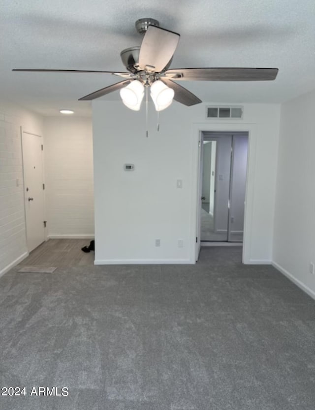 unfurnished room with ceiling fan, a textured ceiling, and dark colored carpet