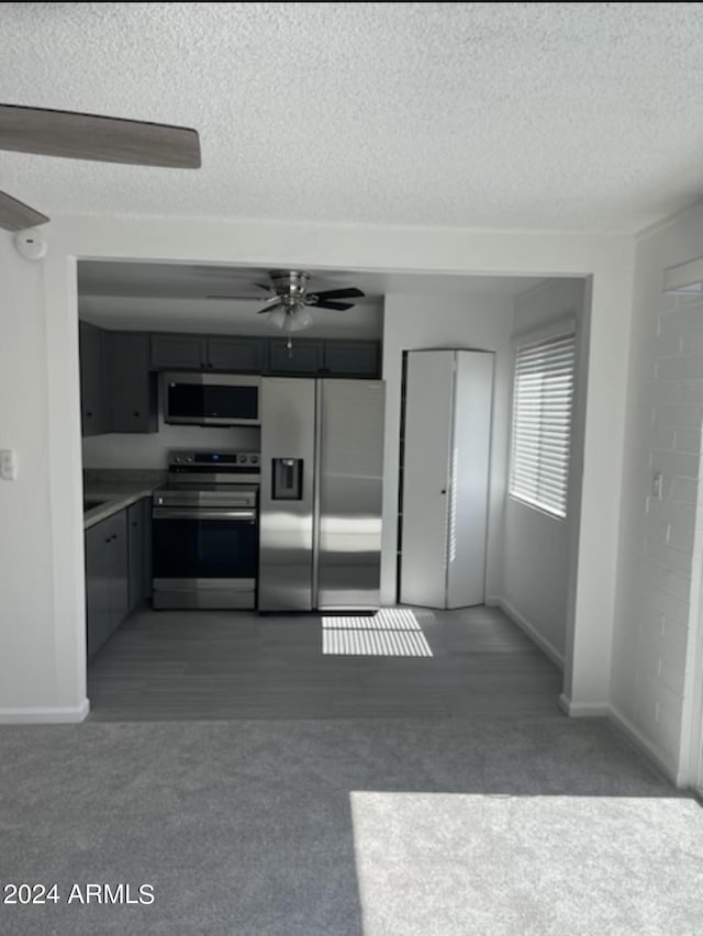 kitchen featuring dark colored carpet, ceiling fan, stainless steel appliances, and a textured ceiling