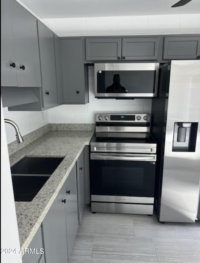 kitchen with stainless steel appliances, gray cabinetry, and sink