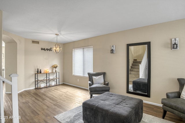 living area with wood finished floors, visible vents, arched walkways, stairs, and a chandelier