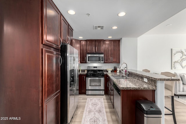 kitchen with sink, a kitchen breakfast bar, kitchen peninsula, dark stone counters, and appliances with stainless steel finishes