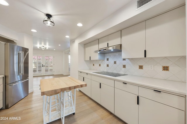 kitchen with stainless steel refrigerator, black electric cooktop, white cabinets, and light hardwood / wood-style flooring