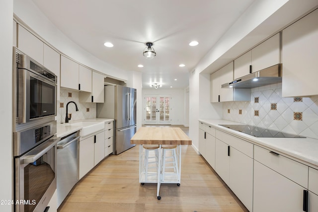 kitchen with appliances with stainless steel finishes, backsplash, sink, light hardwood / wood-style flooring, and white cabinetry