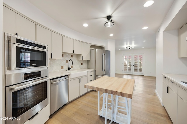 kitchen with backsplash, stainless steel appliances, sink, light hardwood / wood-style floors, and white cabinetry