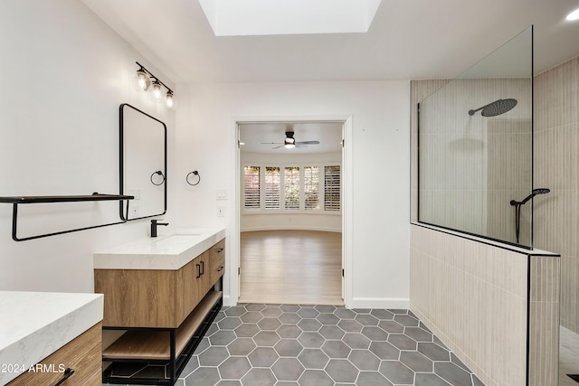 bathroom featuring a tile shower, a skylight, ceiling fan, hardwood / wood-style floors, and vanity