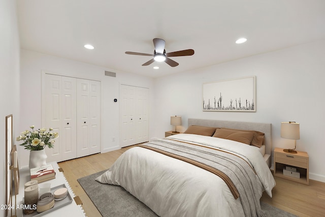 bedroom featuring ceiling fan, light hardwood / wood-style flooring, and two closets