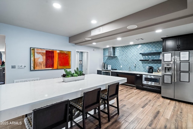 2511 W Queen Creek Rd Unit 116, Chandler, AZ 85248 - kitchen with stainless steel appliances, wall chimney exhaust hood, light countertops, backsplash, and light wood-type flooring