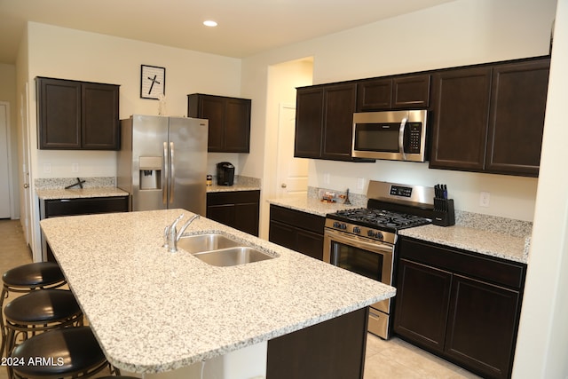 kitchen with dark brown cabinetry, appliances with stainless steel finishes, a kitchen bar, and an island with sink