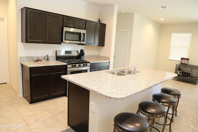 kitchen with sink, appliances with stainless steel finishes, dark brown cabinets, and an island with sink