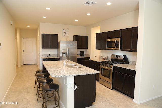 kitchen with sink, light tile patterned flooring, stainless steel appliances, dark brown cabinetry, and a center island with sink