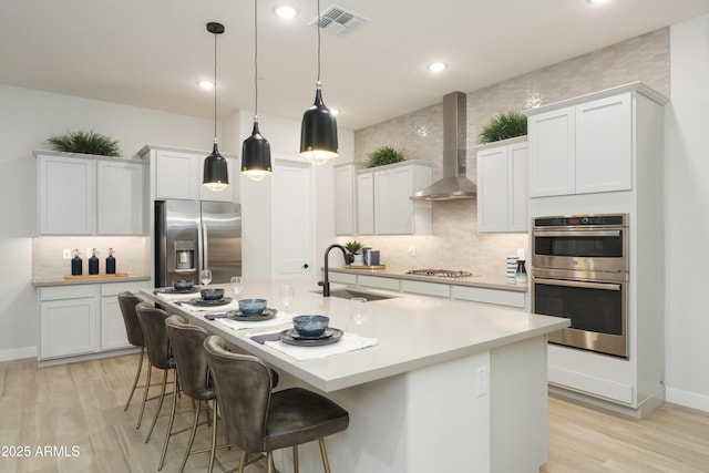 kitchen featuring wall chimney exhaust hood, sink, white cabinetry, and stainless steel appliances