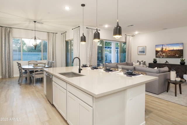 kitchen featuring a kitchen island with sink, sink, dishwasher, a notable chandelier, and white cabinets