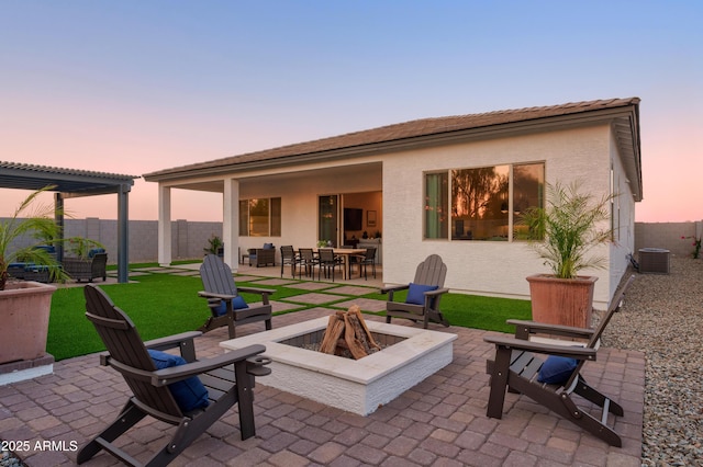 back house at dusk featuring a pergola, central AC, a patio, and a fire pit