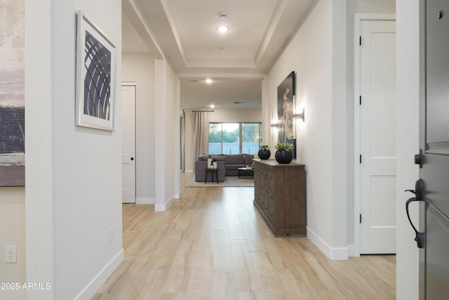 hallway featuring a tray ceiling and light hardwood / wood-style flooring