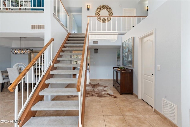 stairway featuring tile patterned floors, a towering ceiling, visible vents, and baseboards