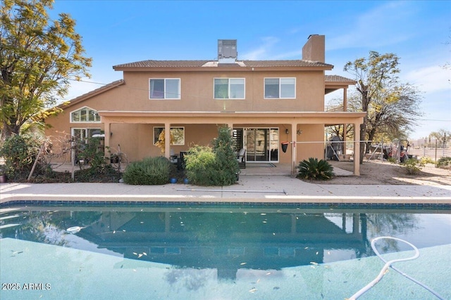 rear view of property featuring a patio area, a chimney, an outdoor pool, and stucco siding