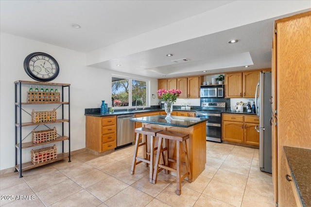 kitchen featuring a raised ceiling, appliances with stainless steel finishes, a breakfast bar, a center island, and a sink