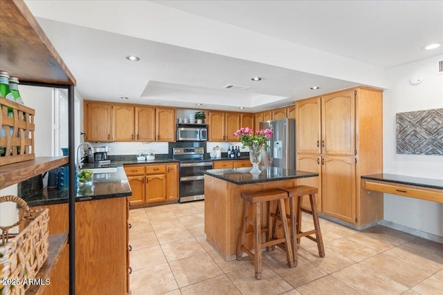kitchen featuring a sink, appliances with stainless steel finishes, a center island, dark stone countertops, and a raised ceiling