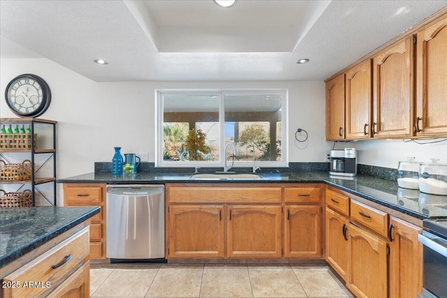 kitchen with a sink, stainless steel dishwasher, range, dark stone countertops, and a raised ceiling