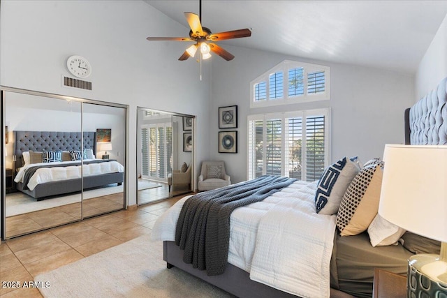 bedroom with two closets, light tile patterned floors, visible vents, ceiling fan, and vaulted ceiling