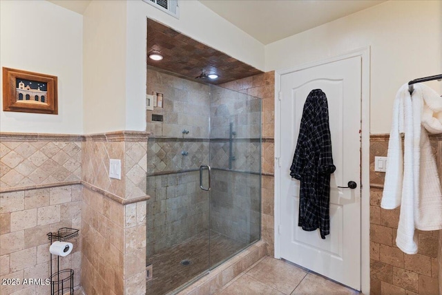 bathroom featuring visible vents, a stall shower, wainscoting, and tile walls