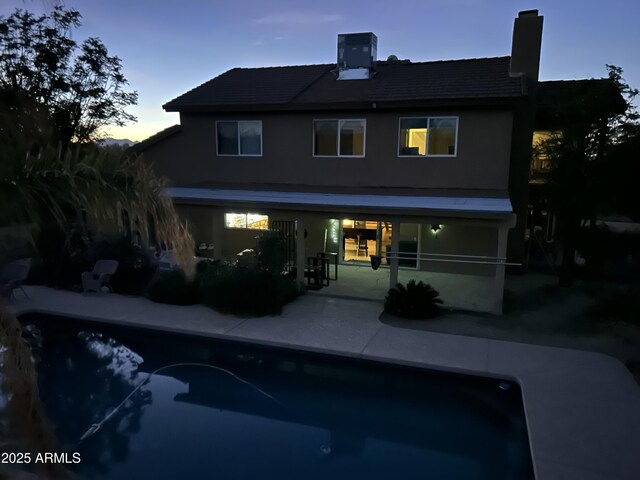 back of property at dusk with a chimney, an outdoor pool, central AC, and a patio