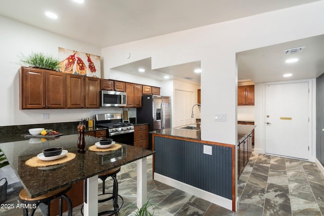 kitchen featuring kitchen peninsula, sink, appliances with stainless steel finishes, a kitchen breakfast bar, and dark stone counters