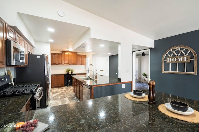 kitchen with ceiling fan, a center island, sink, stainless steel appliances, and dark stone counters