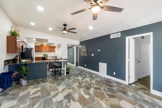 kitchen with vaulted ceiling, a kitchen breakfast bar, kitchen peninsula, stainless steel refrigerator, and ceiling fan