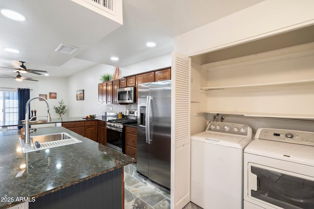 kitchen with ceiling fan, washer and dryer, dark stone countertops, sink, and appliances with stainless steel finishes