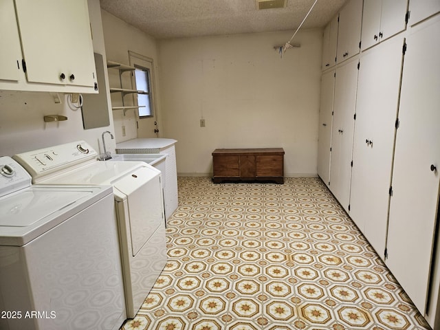 clothes washing area featuring visible vents, cabinet space, a textured ceiling, and washing machine and clothes dryer