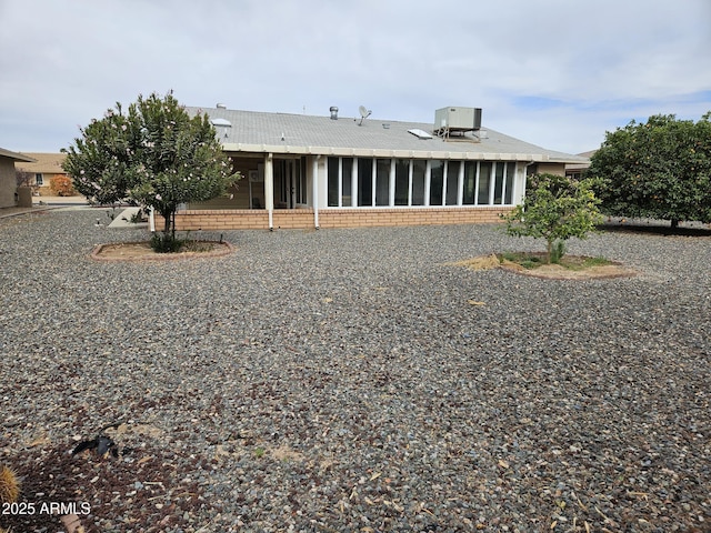 back of property featuring a sunroom, brick siding, and central AC unit