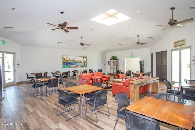 dining space featuring ceiling fan, vaulted ceiling with skylight, and light hardwood / wood-style flooring