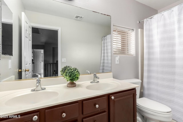 bathroom with toilet, double vanity, visible vents, and a sink