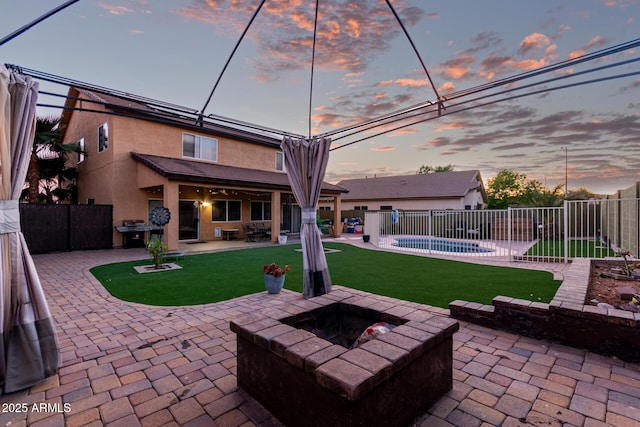 rear view of property with a fire pit, a patio area, a fenced in pool, and stucco siding