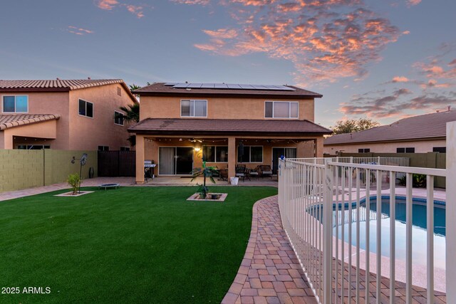 rear view of house with solar panels, a patio area, a fenced backyard, and a fenced in pool