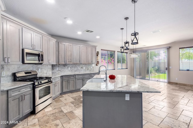 kitchen featuring gray cabinetry, hanging light fixtures, stainless steel appliances, decorative backsplash, and a center island with sink