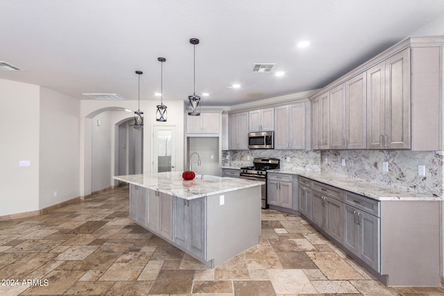 kitchen with appliances with stainless steel finishes, decorative light fixtures, backsplash, and an island with sink