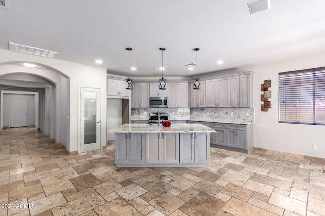 kitchen with decorative backsplash, an island with sink, light stone countertops, decorative light fixtures, and stainless steel appliances