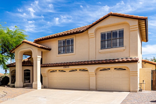 mediterranean / spanish-style home with fence, stucco siding, a tiled roof, concrete driveway, and an attached garage