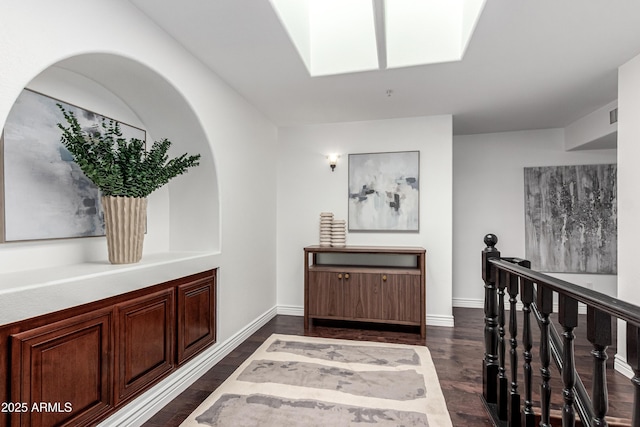 hallway featuring baseboards, dark wood-style floors, a skylight, and visible vents