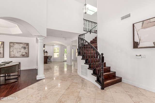 foyer entrance with visible vents, arched walkways, stairs, baseboards, and ornate columns