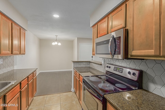 kitchen featuring a notable chandelier, hanging light fixtures, stainless steel appliances, light tile patterned floors, and dark stone countertops