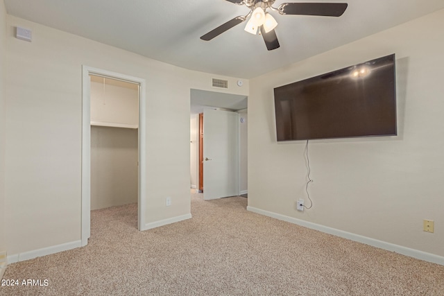 unfurnished bedroom with ceiling fan, a closet, light carpet, and a walk in closet