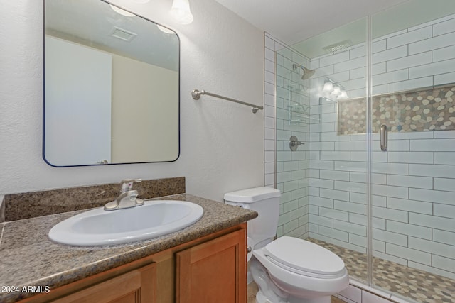 bathroom featuring a shower with door, vanity, and toilet