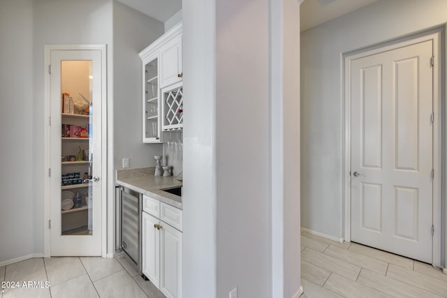 bar with wine cooler, white cabinets, and light stone counters