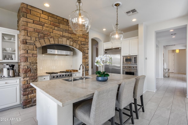 kitchen featuring sink, built in appliances, white cabinetry, and an island with sink