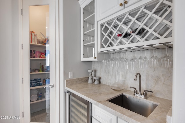 bar featuring white cabinets, sink, beverage cooler, and backsplash